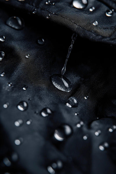The Brown Buffalo-Next-Level Comfort-Water Resistance Close-up of water droplets on a black fabric surface with a brand logo.